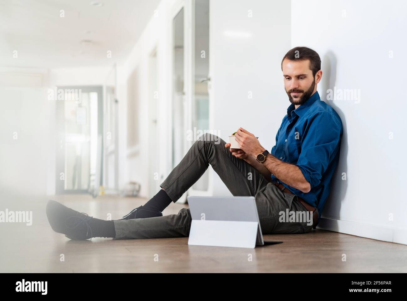 Junger Geschäftsmann, der beim Essen auf ein digitales Tablet schaut Büro Stockfoto