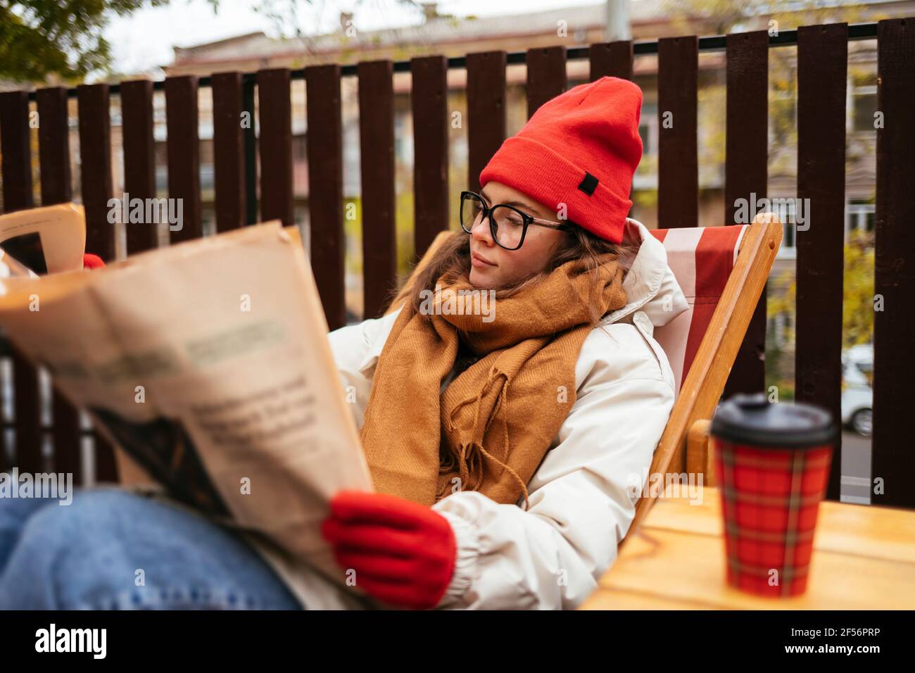 Junge Frau in warmer Kleidung liest Zeitung, während sie sich entspannt Stuhl im Café Stockfoto
