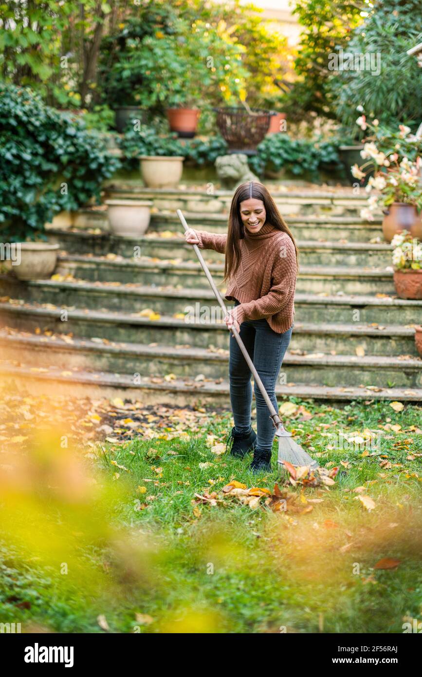 Frau in warmer Kleidung, die mit Rechen im Hinterhof fegen Garten Stockfoto