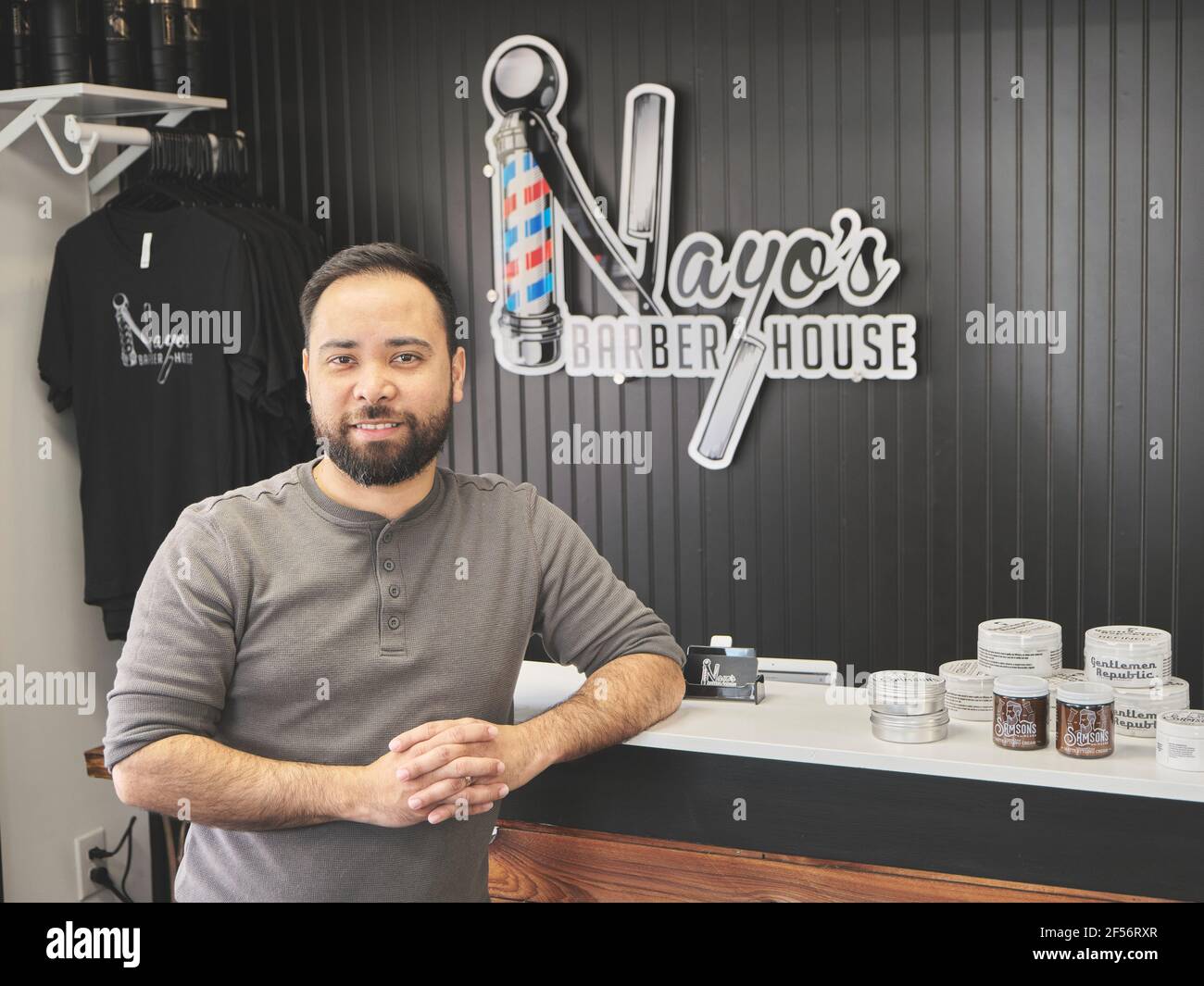 Hispanic Latino, ein männlicher Barbier, der vor seinem Schild oder seinem Logo in seinem Friseurgeschäft in seiner Minderheit in Pike Road Alabama, USA, steht. Stockfoto