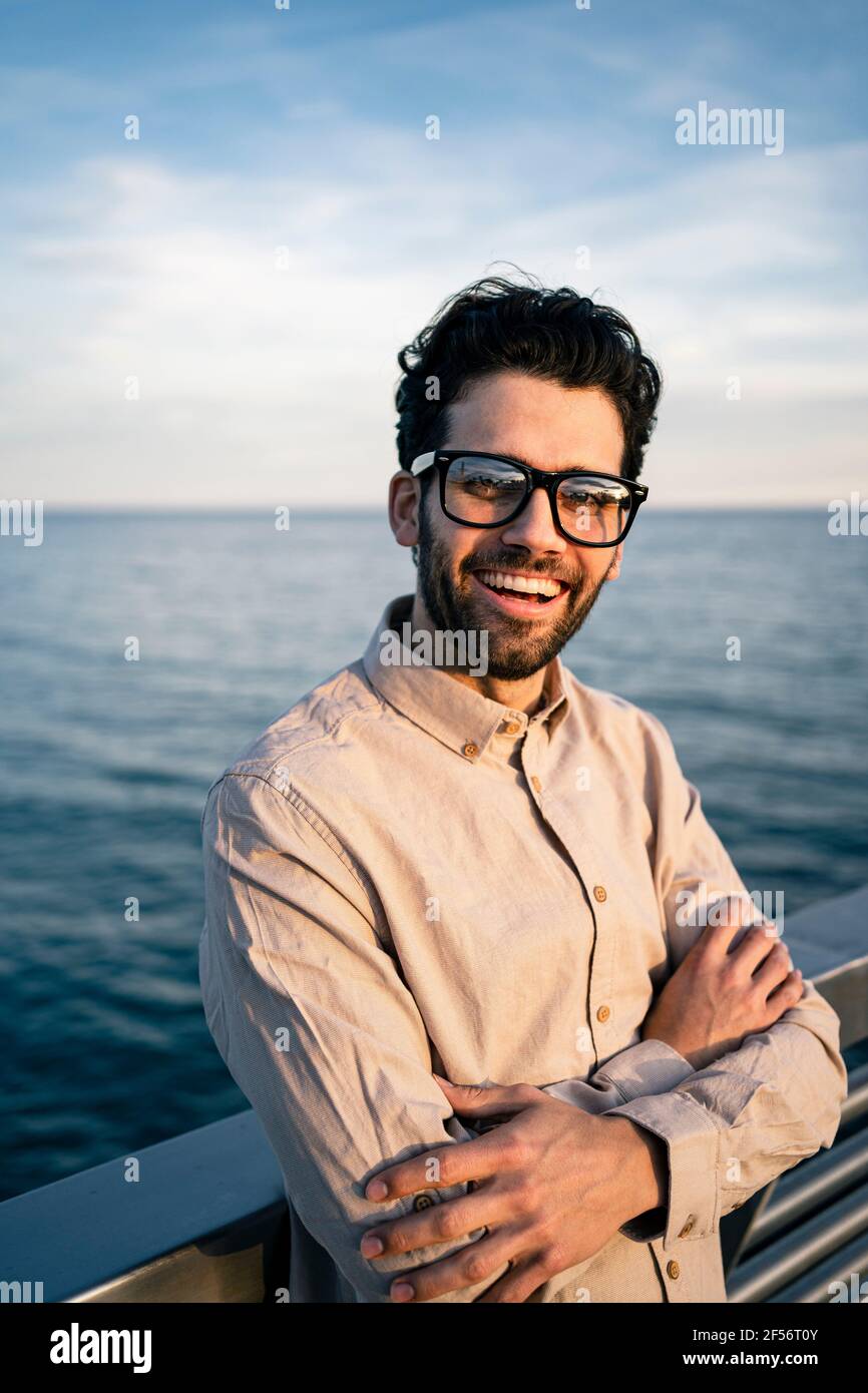 Glücklicher Geschäftsmann mit gekreuzten Armen, die am Meer stehen Stockfoto