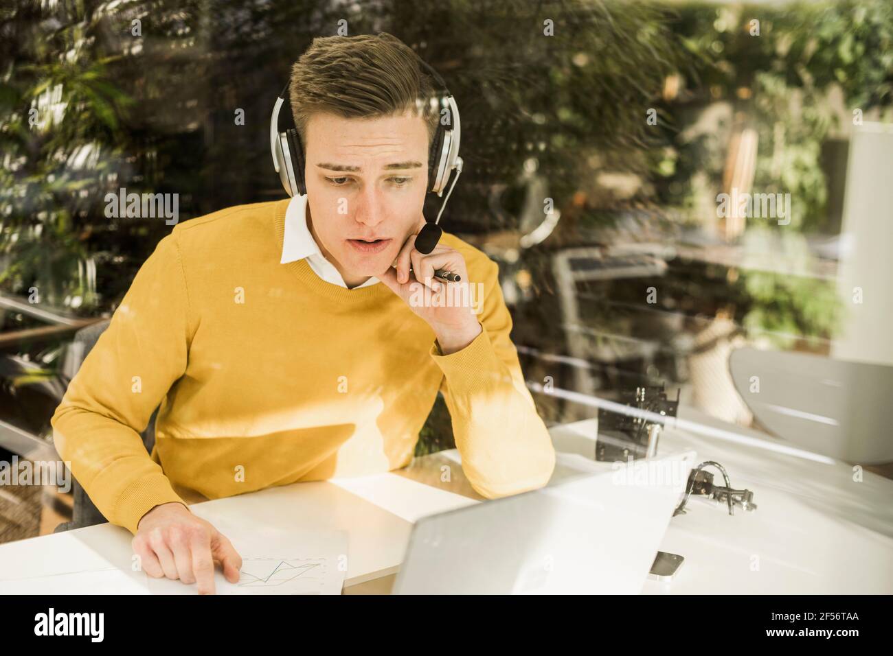 Junger Profi mit Kopfhörern, der zu Hause an einem Geschäftstreffen teilnimmt Büro Stockfoto