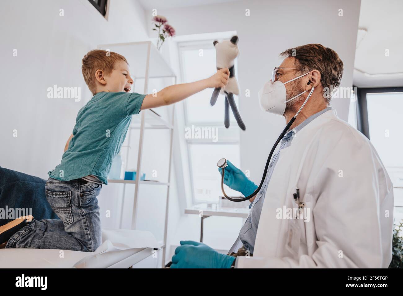 Hausarzt untersucht spielerischen Jungen spielen mit Spielzeug in der Untersuchung Zimmer Stockfoto