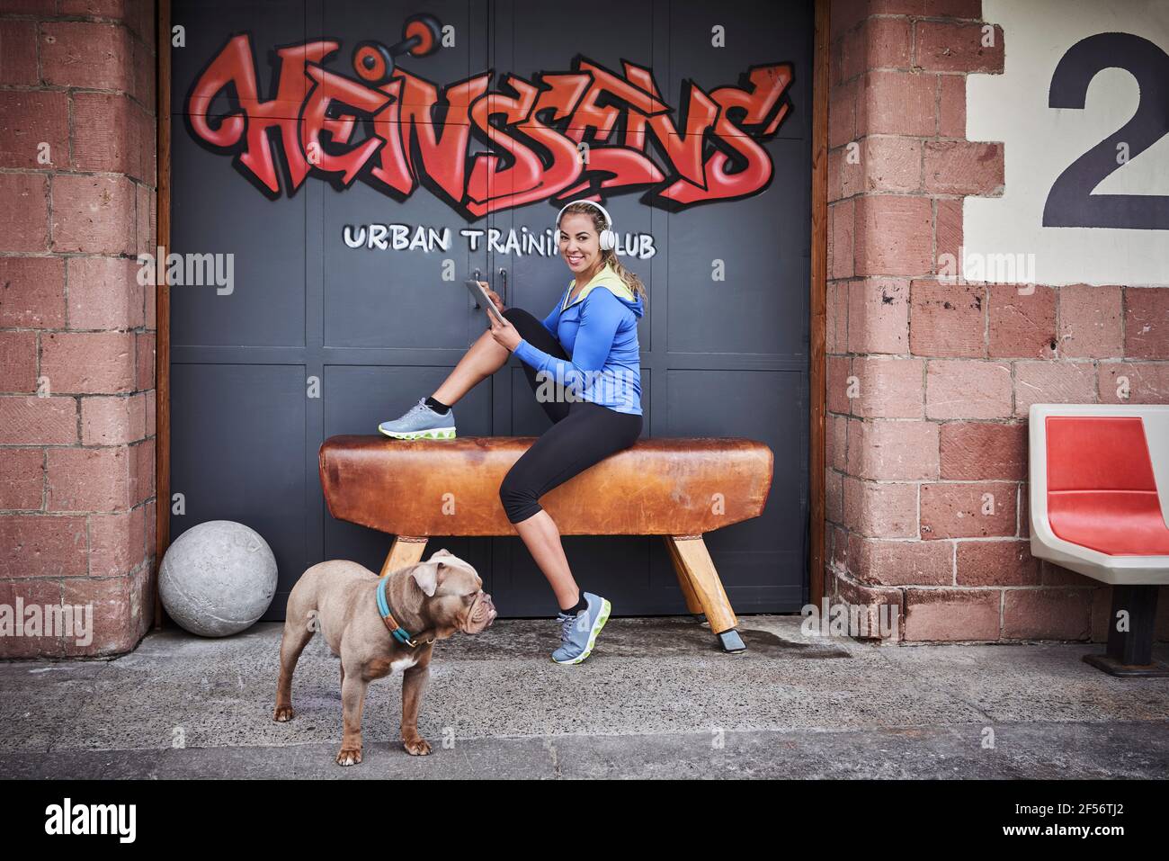 Lächelnde Sportlerin mit digitalem Tablet, das auf der Bank gegen Graffiti sitzt Tür Stockfoto