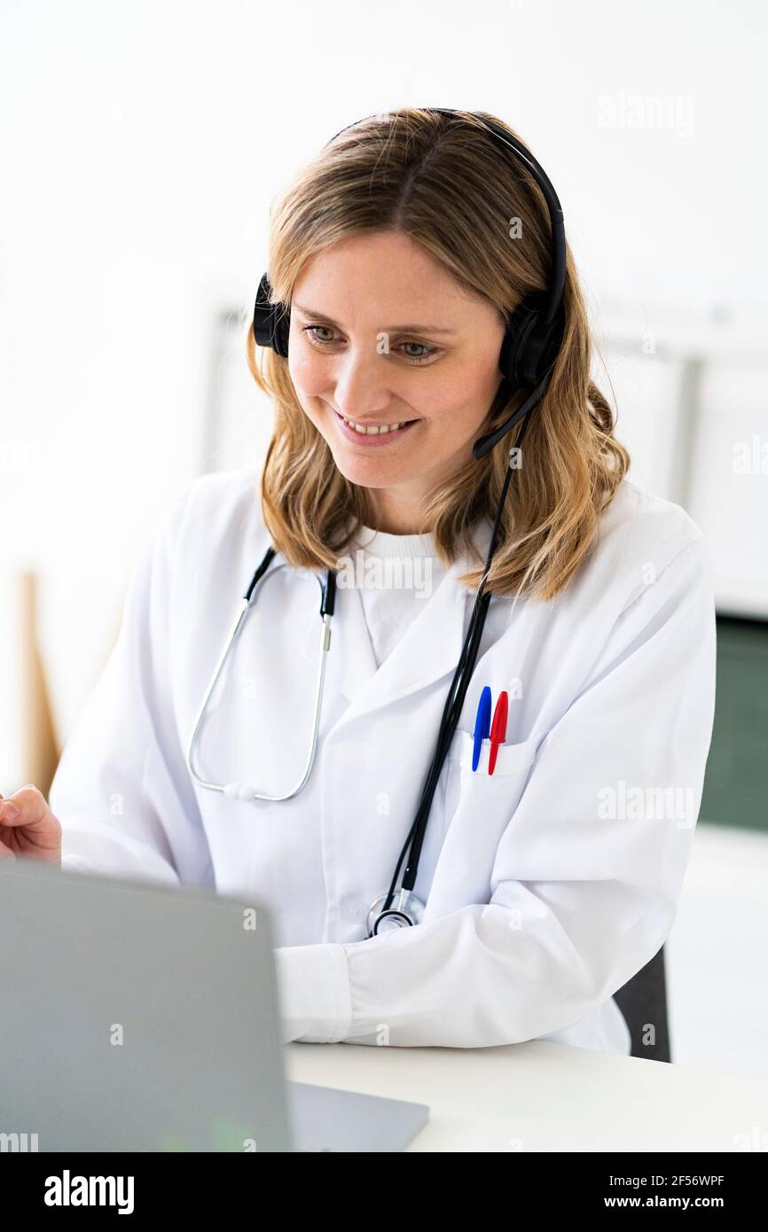 Lächelnde Ärztin, die Online-Konsultation über Laptop in medizinischen Klinik Stockfoto