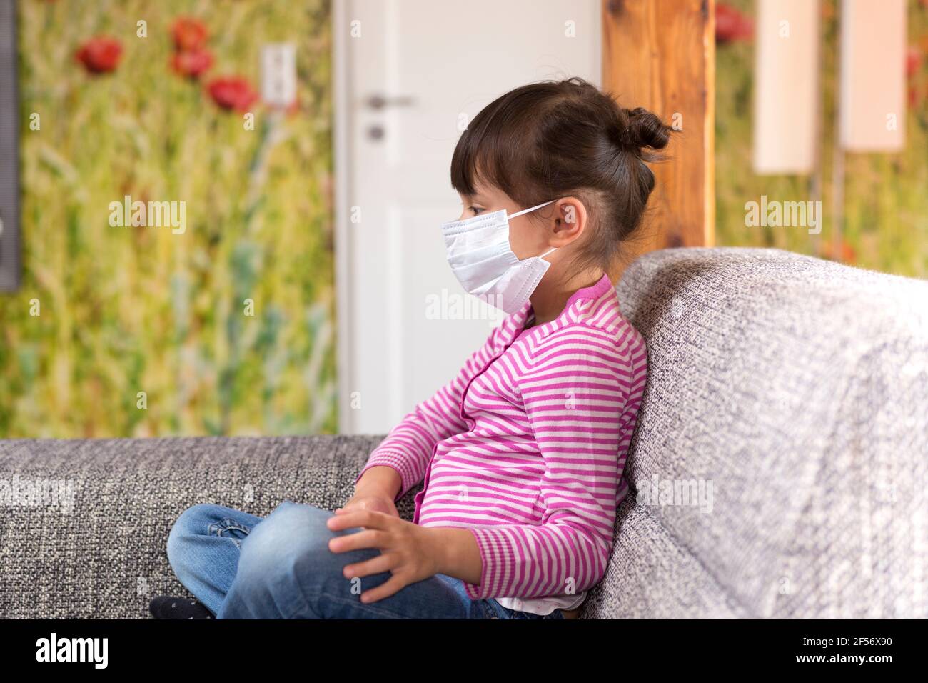 Kind sitzt auf der Couch in Gesichtsmaske Stockfoto