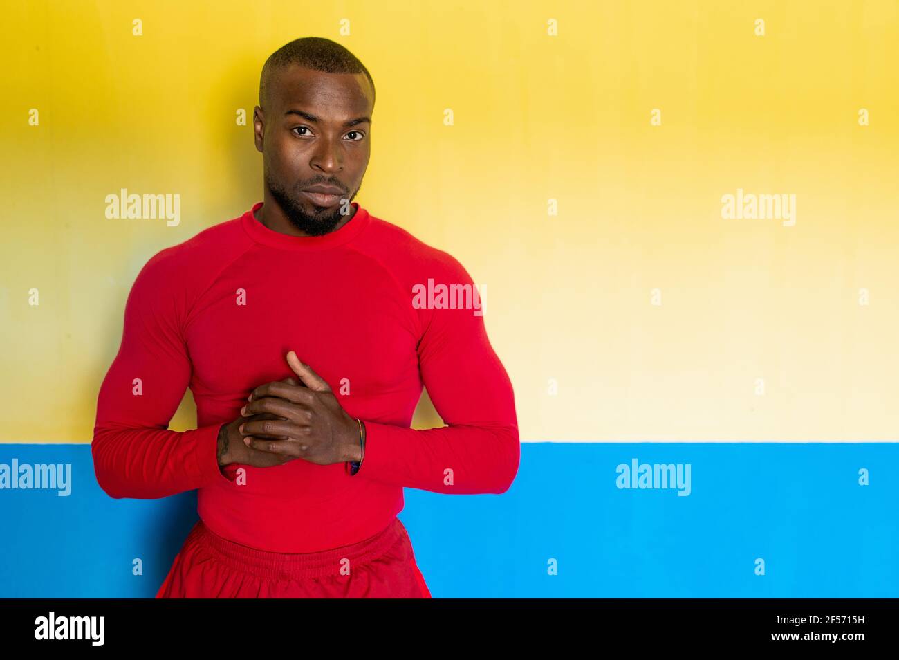 Afrikanischer sportlicher Mann mit perfektem Körper, der auf die Kamera schaut, mit ernsthaftem Gesicht und Händen, die in gelbem Hintergrund geklammt sind. Stockfoto