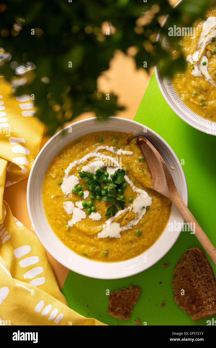 Vegetarische Butternut-Kürbis-Sahne-Suppe garniert mit frischen grünen Erbsen Und Petersilienblätter auf leuchtend gelbem und grünem Hintergrund Stockfoto