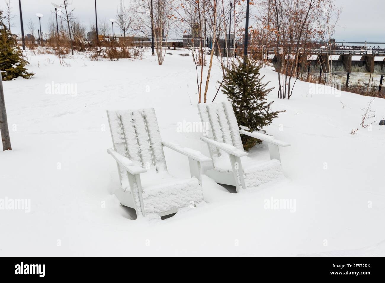 Weiße, schneebedeckte Holzstühle mit Blick auf eisige Stromschnellen von den Chaudière Falls (auch bekannt als Akikodjiwan) in Ottawa, Kanada Stockfoto