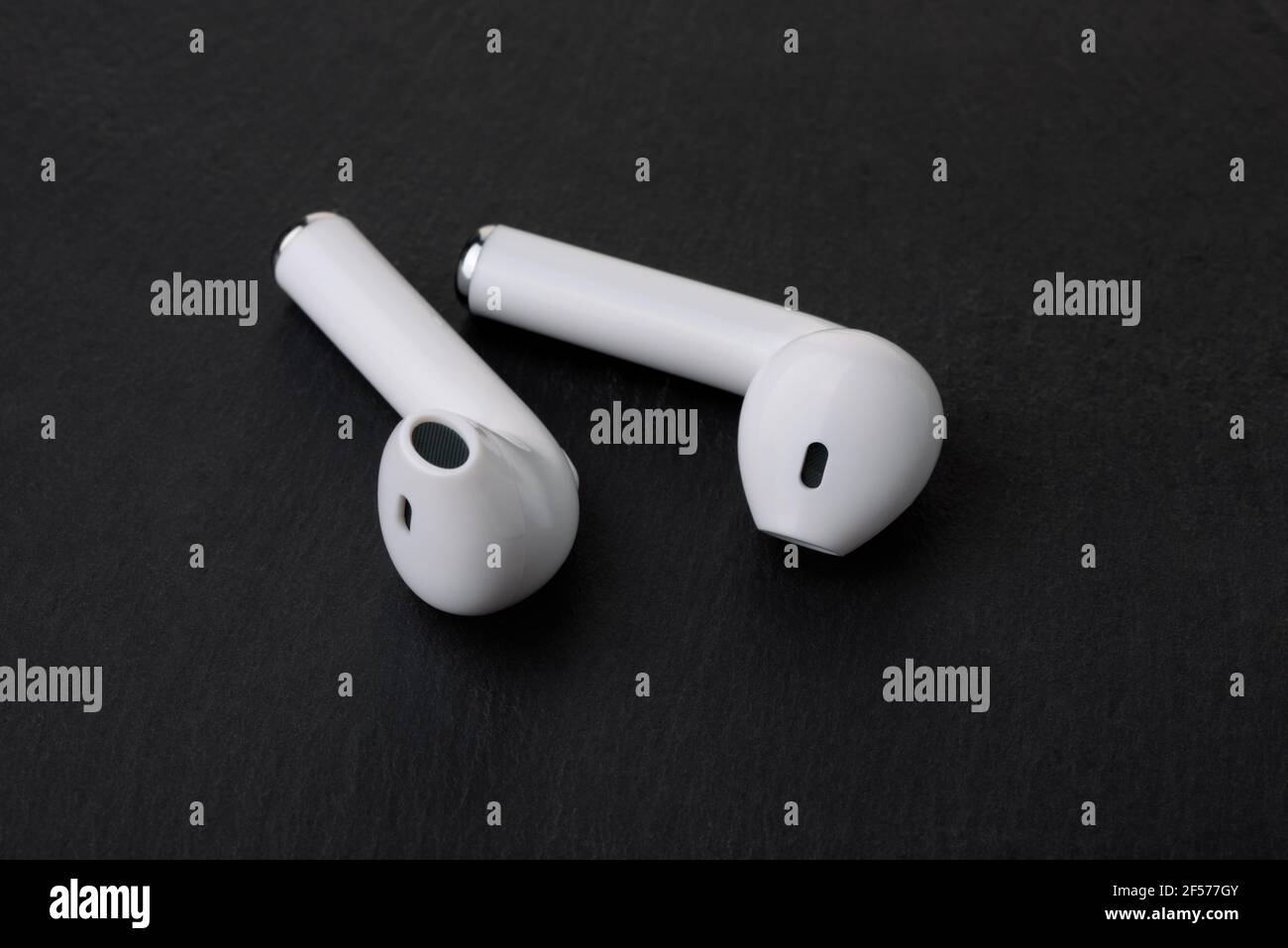 Ein Paar weiße, schnurlose Ohrhörer auf schwarzem Steinhintergrund Stockfoto