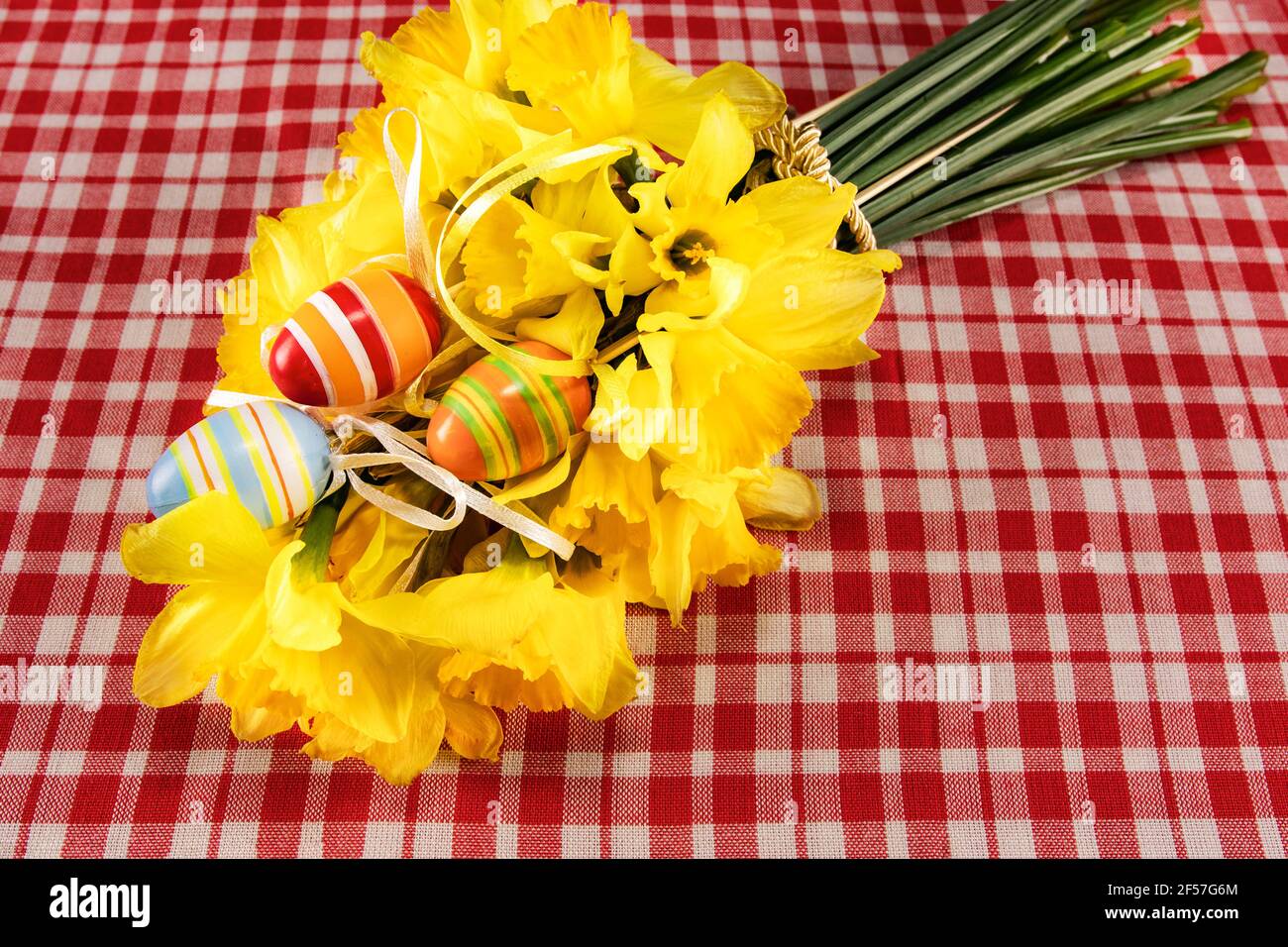 Festliche Osterkarte. Osterstrauß aus gelben Narzissen und handbemalten Eiern auf einem Tisch mit karierter Tischdecke. Ort für Ihren Text. Frühlingsbouq Stockfoto