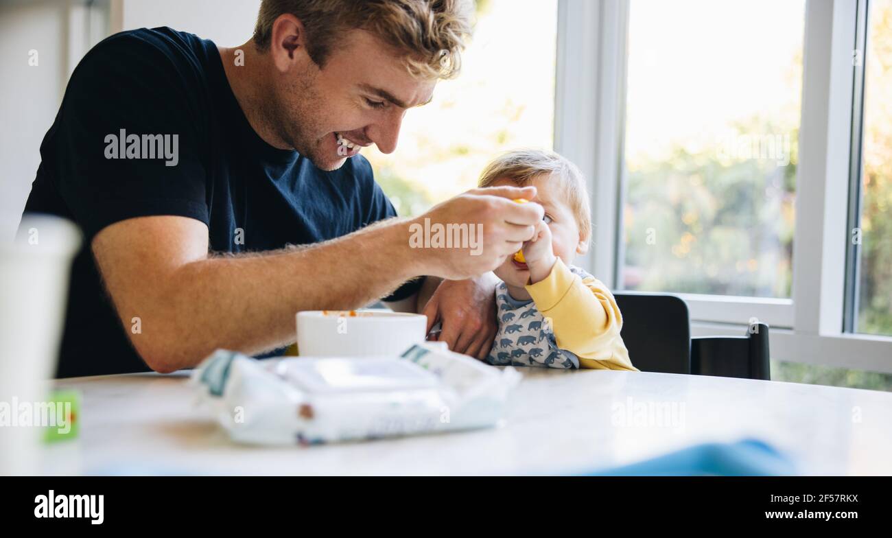 Liebevoller Vater füttert sein Baby mit einem Löffel, während auf Vaterschaft verlassen. Mann Löffel Fütterung sein kleines Baby während Vaterschaftsurlaub. Stockfoto