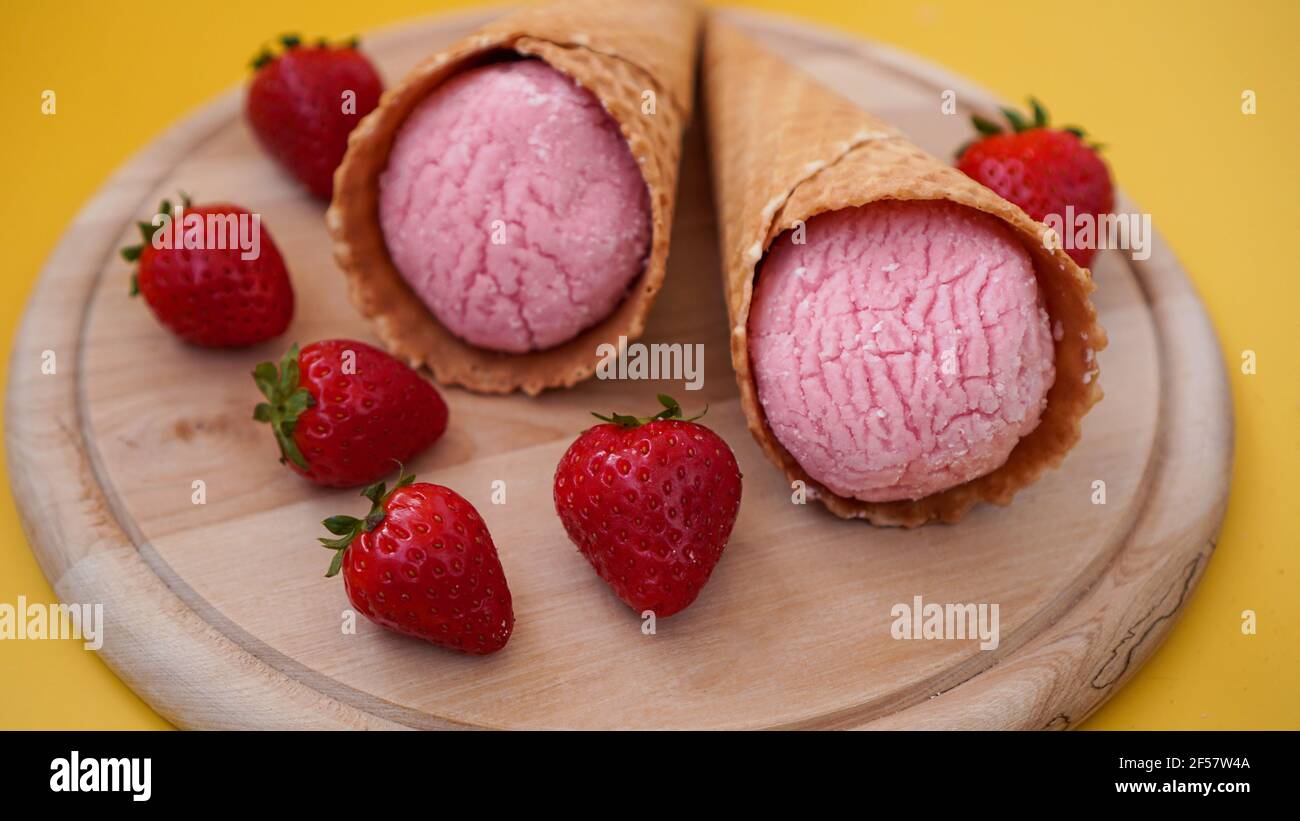 Erdbeereis in einem Waffelkegel. Eis und Beeren auf einem gelben Stockfoto