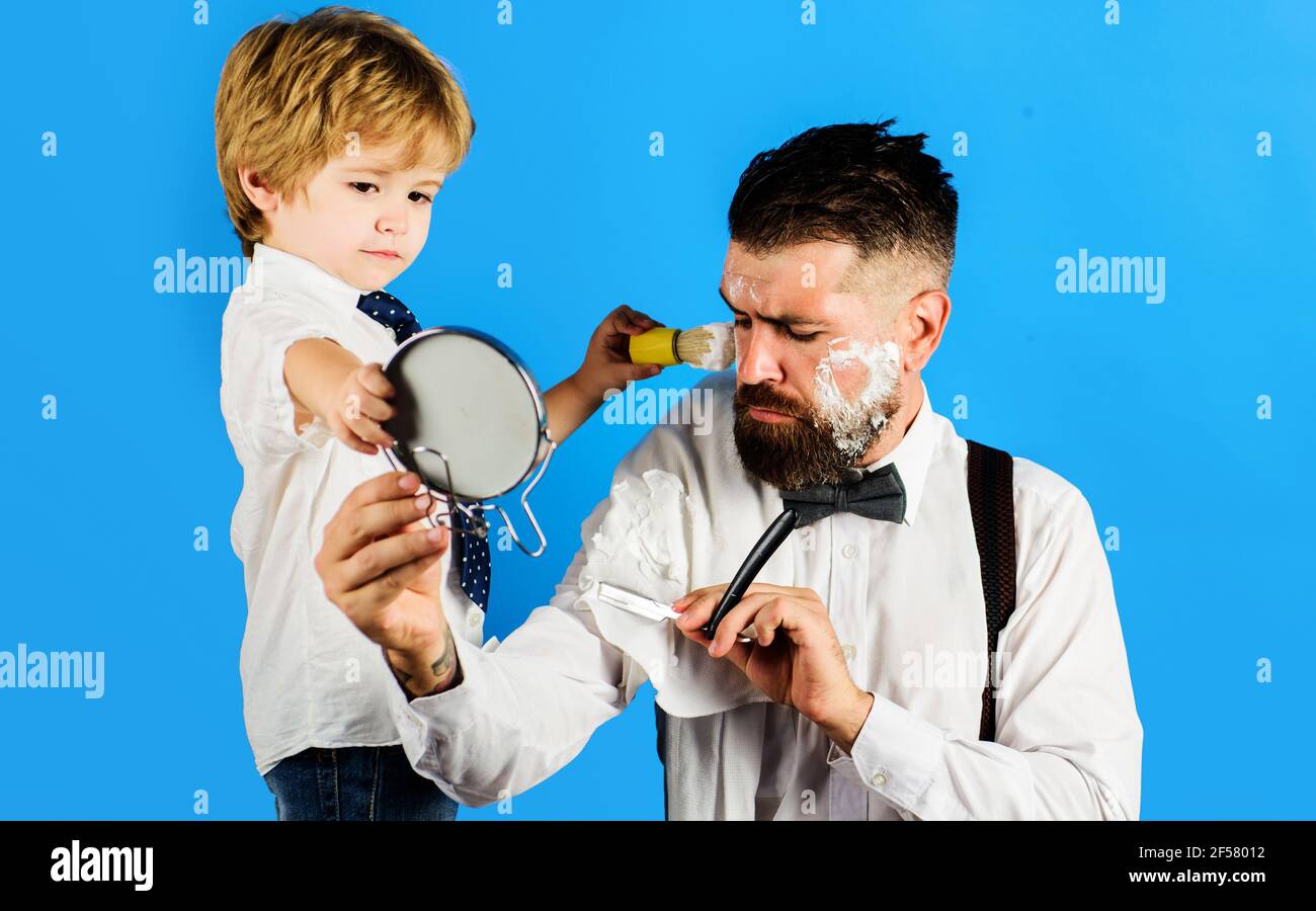 Kleiner Barbier. Assistent für Papa. Vatertag. Sohn hält Spiegel für Vater. Stockfoto