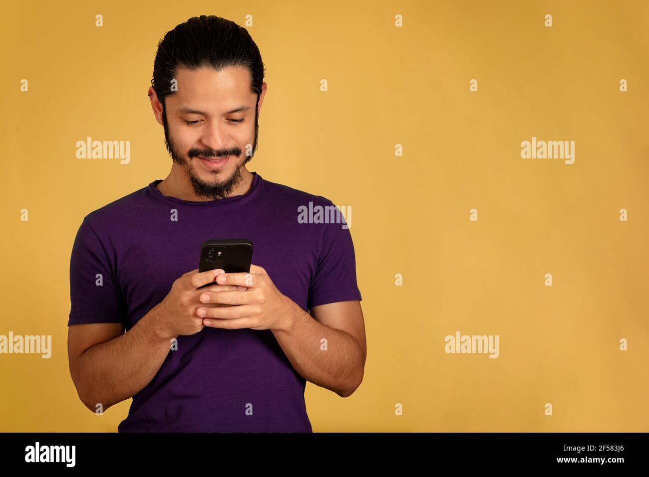 Junger Mann SMS und spielen mit dem Smartphone. Gelber Hintergrund. Stockfoto