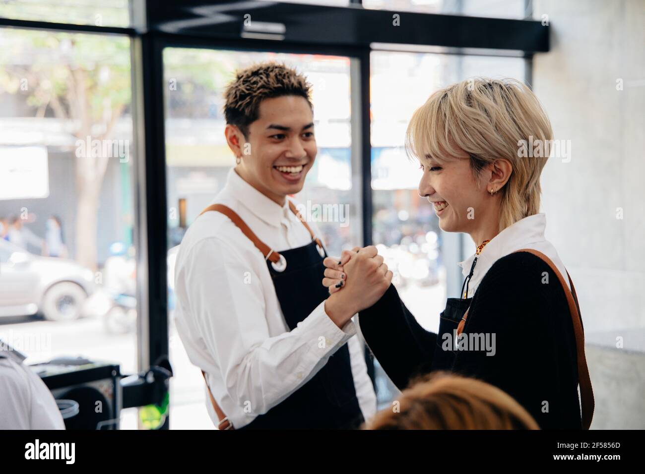 Fröhliche junge asiatische Mann und Frau Friseur trägt Schürze Uniform Im modernen Salon geben High-fünf einander auf feiern Erfolg des Salons Stockfoto