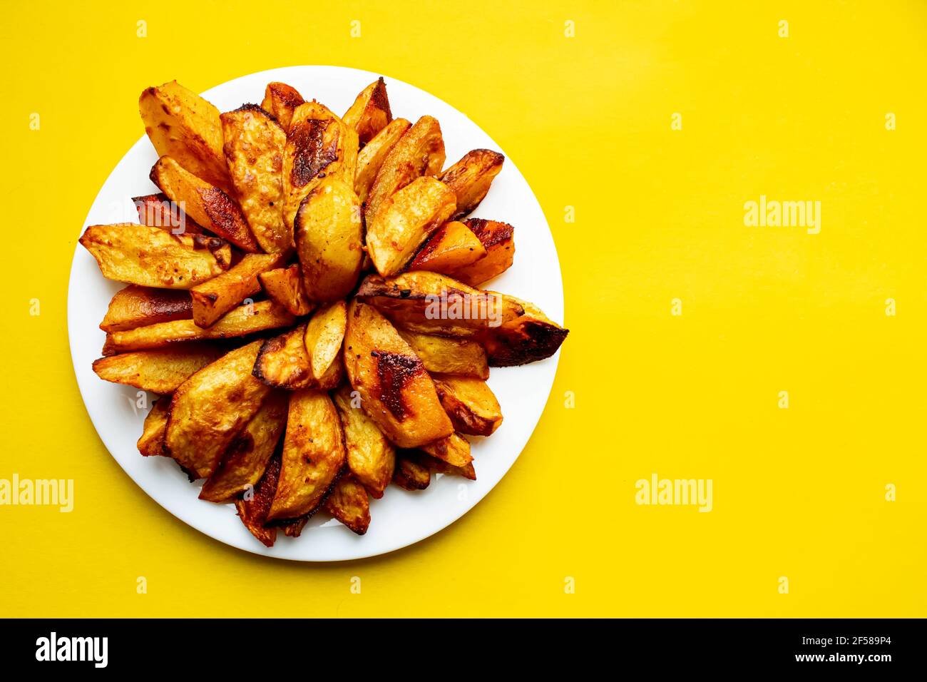 Gebratene Pommes und Tomatensauce auf gelbem Hintergrund. Fast Food. Rustikale Kartoffeln im Ofen gebacken. In Scheiben geschnittene und gebratene Kartoffeln. Stockfoto