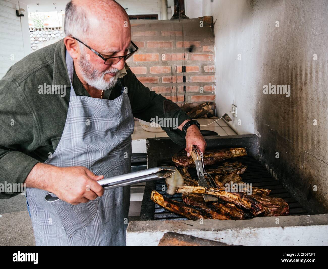 OL Mann Kochen Tomahawk Rib Beef Steak auf heißen schwarzen Grill Stockfoto