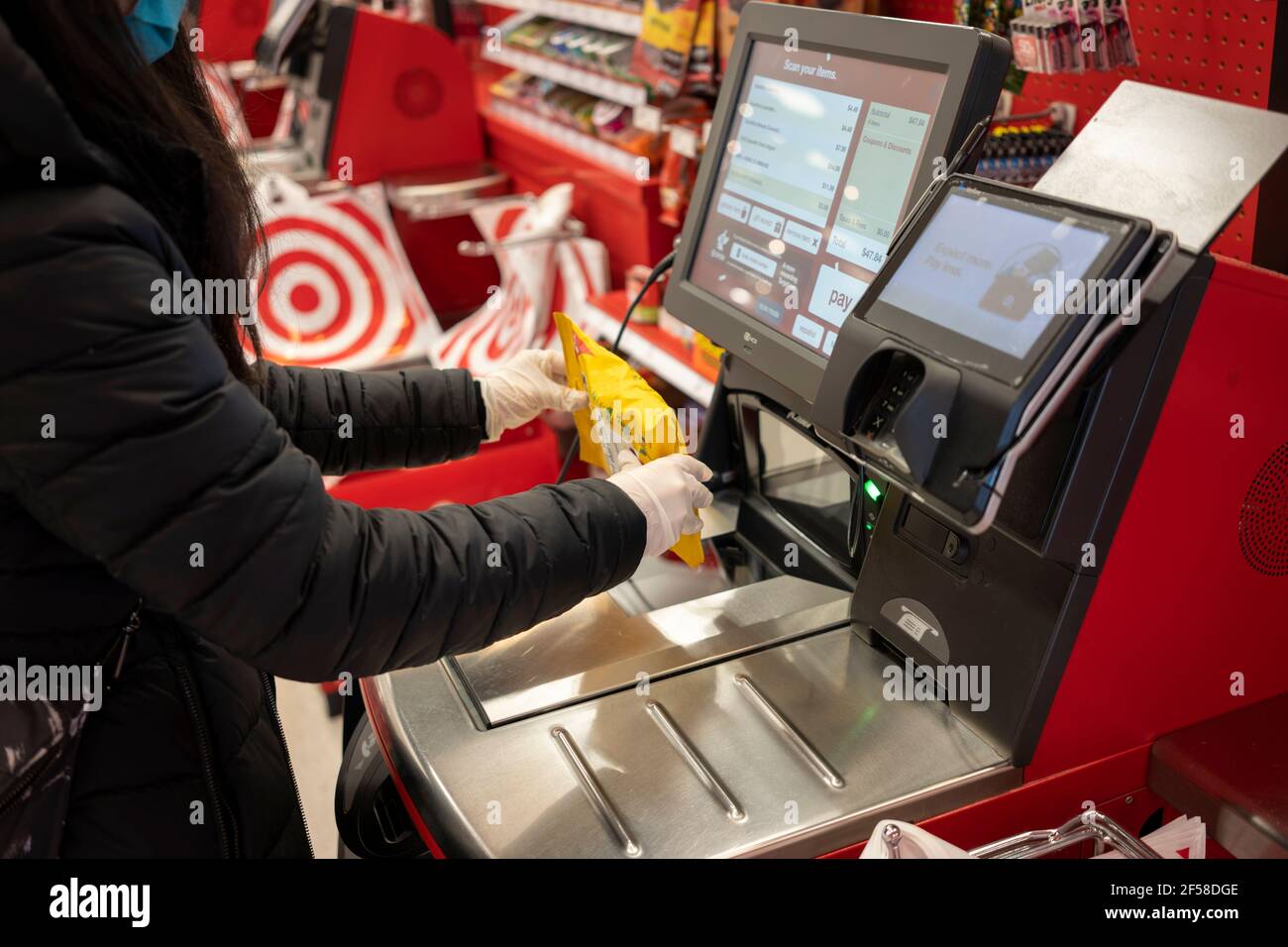 Ein maskierter Shopper mit Nitrilhandschuhen scannt am 21. Februar 2021 in einem Target-Store in Tigard, Oregon, an der Selbstabholspur einen Beutel mit Ricola-Hustenfallen. Stockfoto