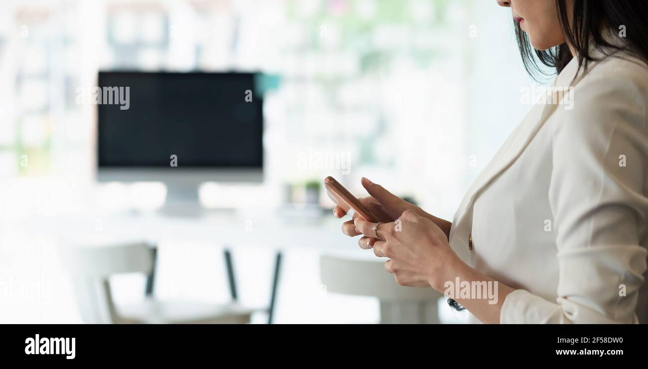 Geschäftsfrau mit Smartphone in ihrem Büro mit Arbeitsplatz Hintergrund Stockfoto