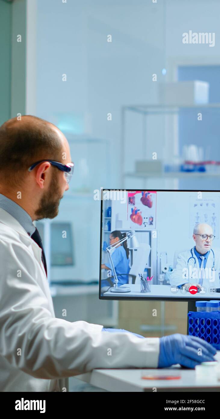 Team von Wissenschaftlern Beratung mit professionellen Arzt auf Video-Anruf, diskutieren während der virtuellen Sitzung im medizinischen Labor. Chemiker untersucht die Entwicklung von Impfstoffen mit Hilfe von Hightech-Forschungsmethoden Stockfoto