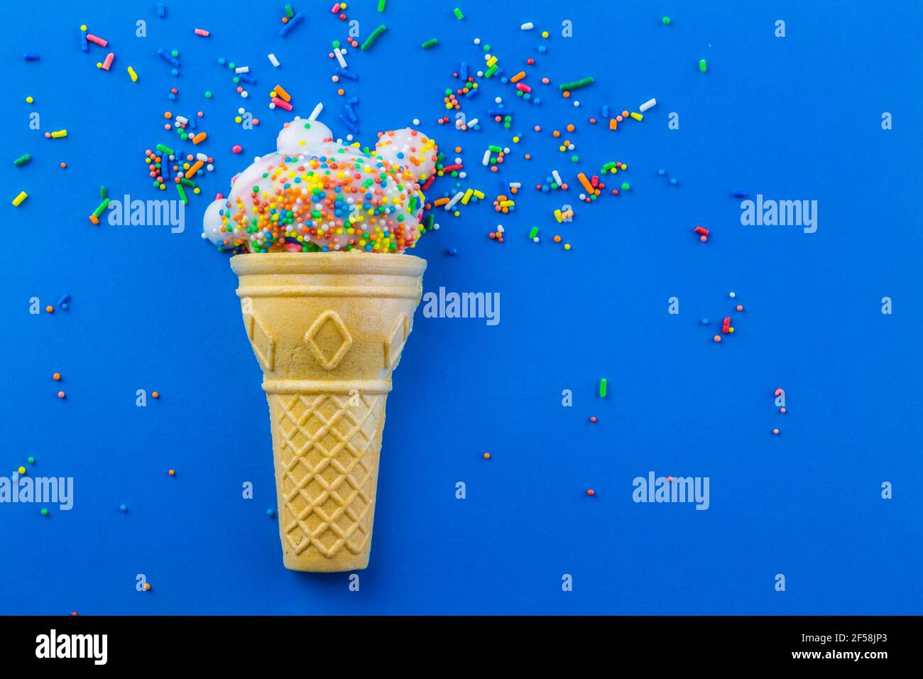 Eiskegel mit kleiner Tasse Kuchen mit Zuckerguss verziert Und runde Streuseln mit Streuseln verstreut und isoliert auf blau Hintergrund - Geburtstag BA Stockfoto