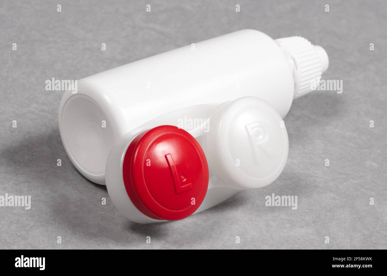 Rotes Kontaktlinsengehäuse und Flasche mit Lösung, isoliert auf grauem Hintergrund Stockfoto