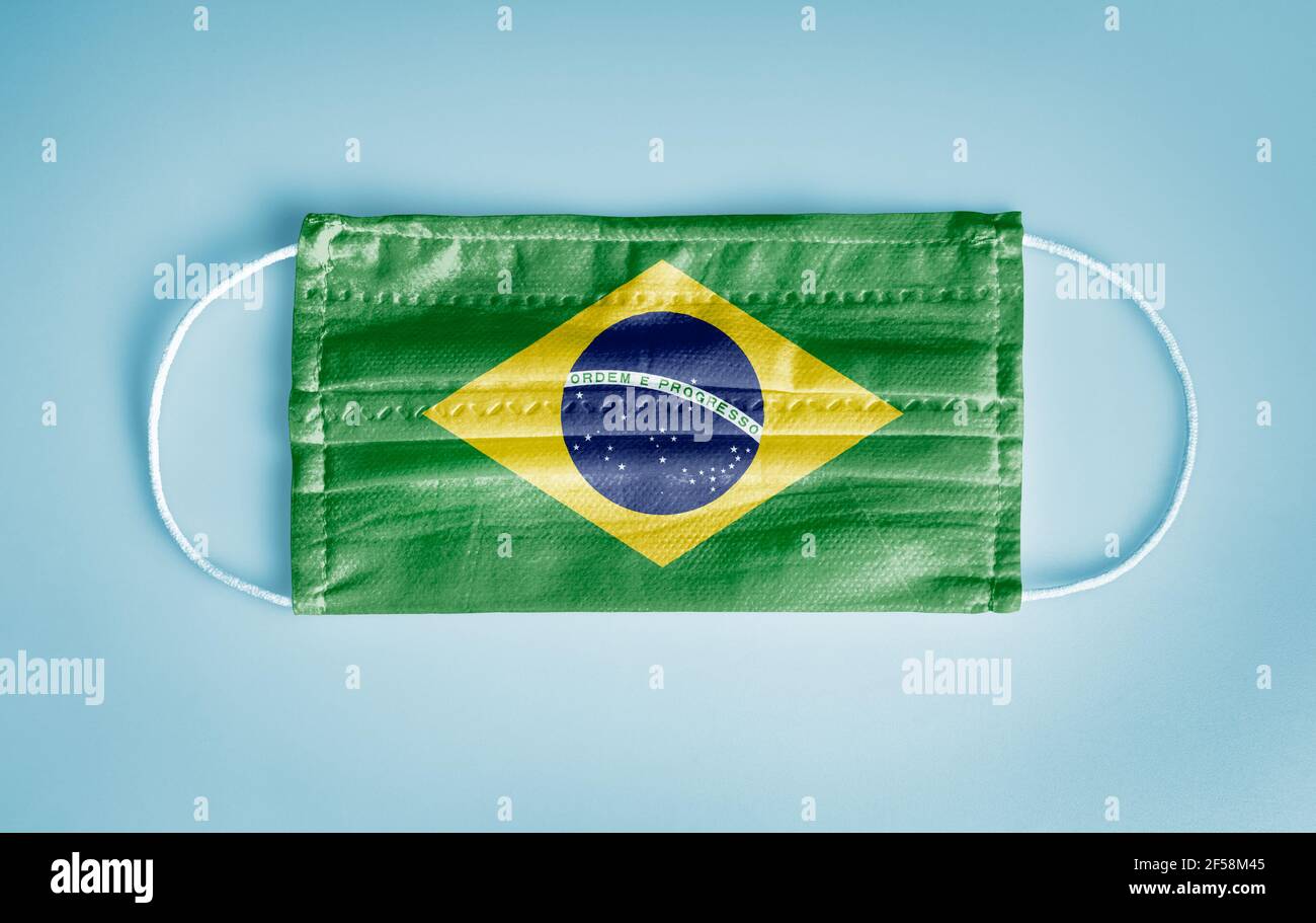 Covid-19 Coronavirus Schutzkonzept: Medizinische Einweg-Gesichtsmaske mit Brasilien Flagge auf blauem Hintergrund. DIE WHO empfiehlt die Verwendung der Maske aus Sicherheitsgründen. Stockfoto