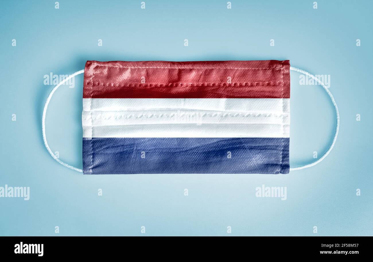 Covid-19 Coronavirus Schutzkonzept: Medizinische Einweg-Gesichtsmaske mit Niederlande Flagge auf blauem Hintergrund. Stockfoto