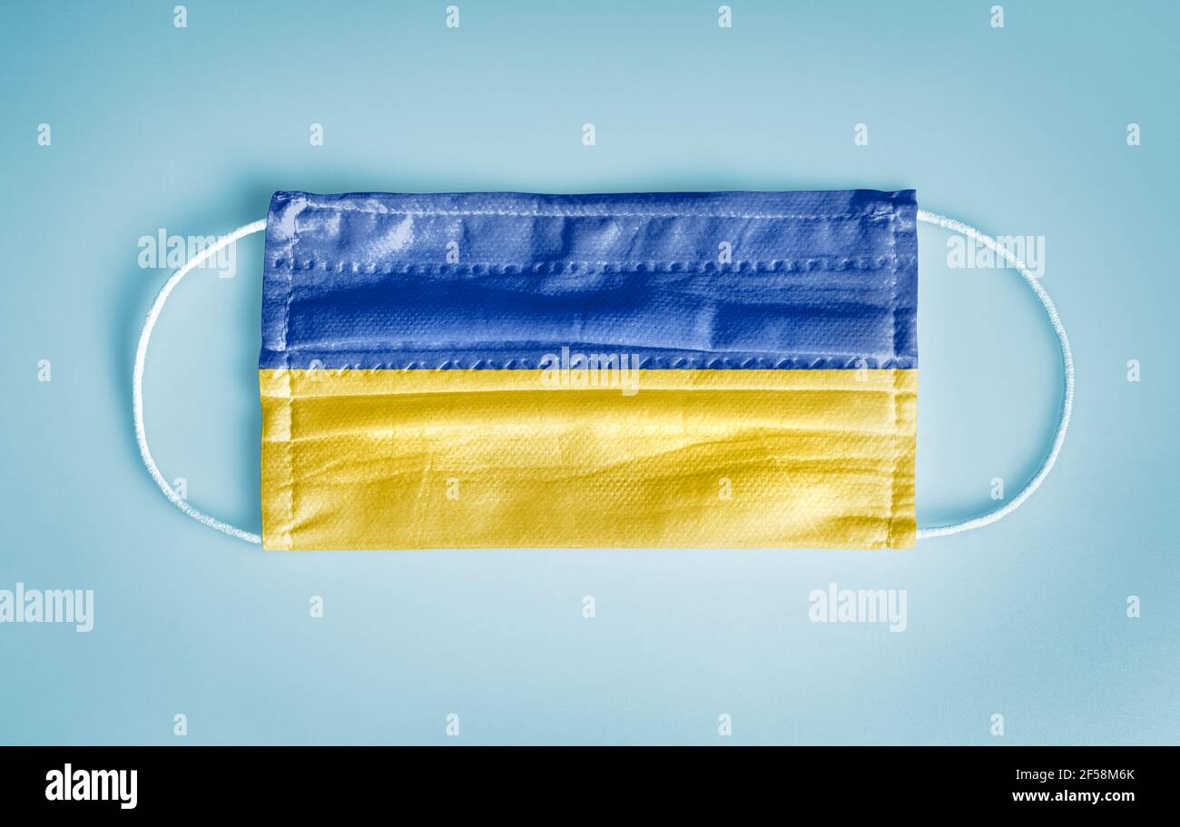 Covid-19 Coronavirus Schutzkonzept: Medizinische Einweg-Gesichtsmaske mit Ukraine-Flagge auf blauem Hintergrund. DIE WHO empfiehlt die Verwendung der Maske aus Sicherheitsgründen. Stockfoto
