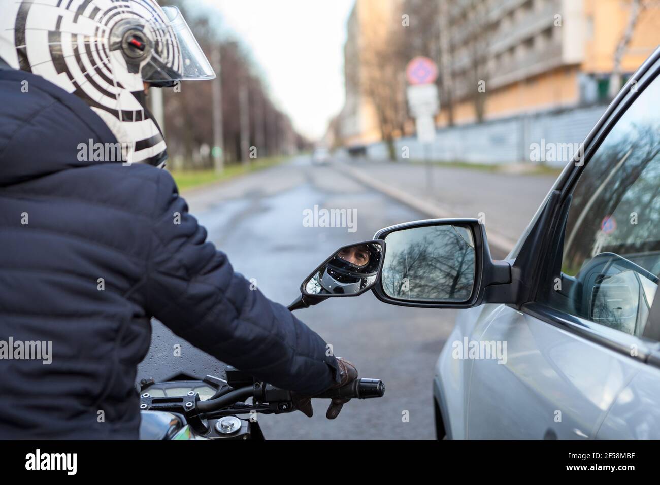 Motorradfahrer steht neben dem Auto auf der Straße, seitliche Rückspiegel sind nah beieinander, berühren während der Bewegung Stockfoto