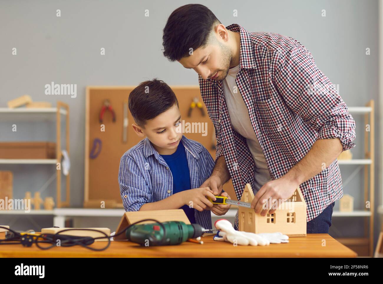 Kleiner Junge und sein Vater machen Holzhaus Modell als Teil des Schulaufgabenprojekts Stockfoto