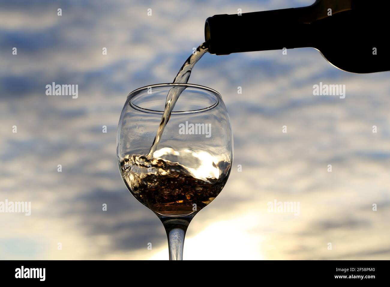 Weißwein, der aus einer Flasche in das Glas gießt, auf einem wunderschönen Hintergrund bei Sonnenuntergang. Konzept der Feier, Sommerparty im Resort, romantisches Abendessen Stockfoto