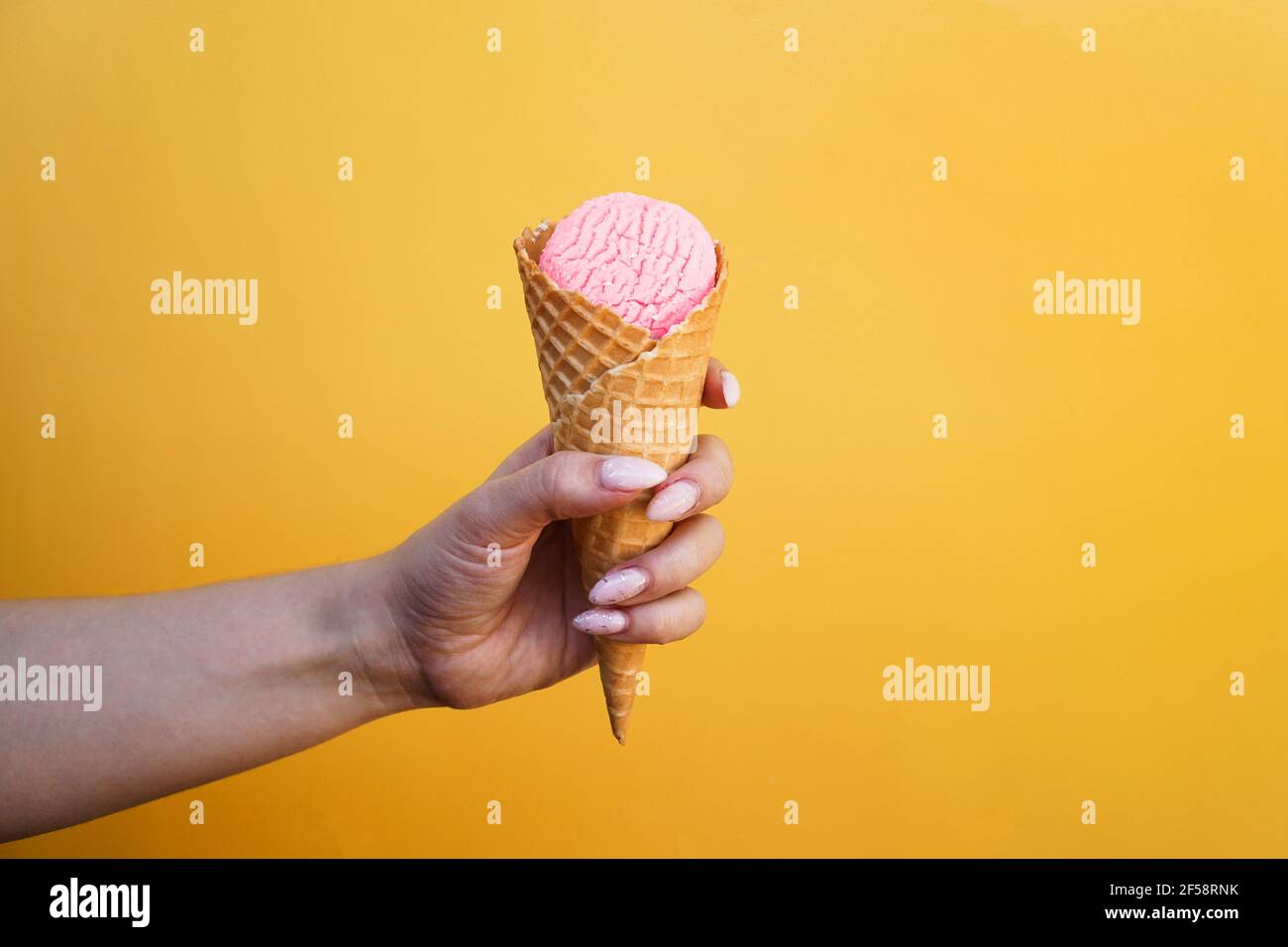 Eis in Waffelbecher in weiblicher Hand auf gelb Hintergrund Stockfoto