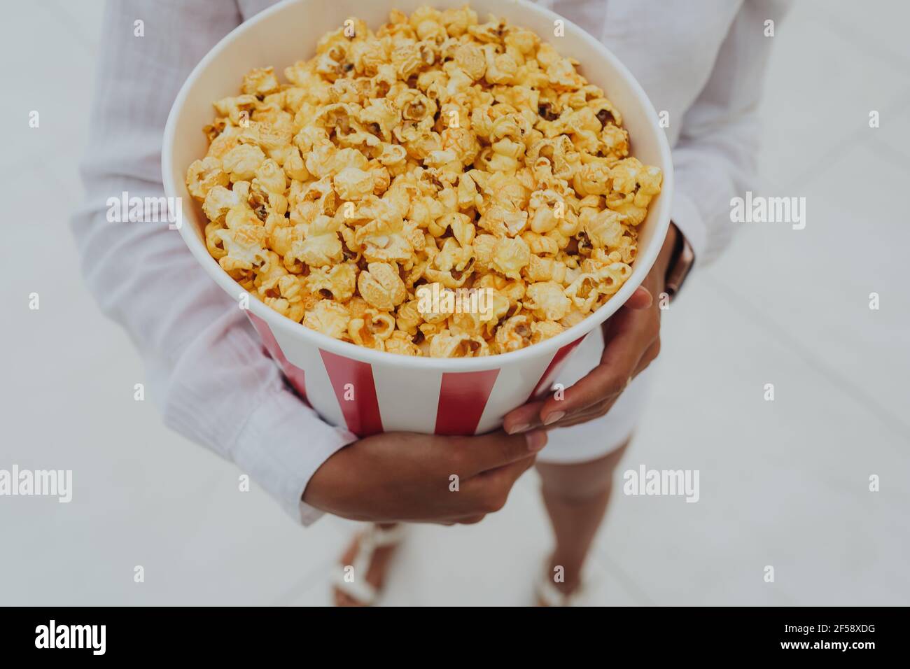 Nahaufnahme eines jungen süßen Mädchens, das eine Tube Popcorn in den Händen hält. Stockfoto