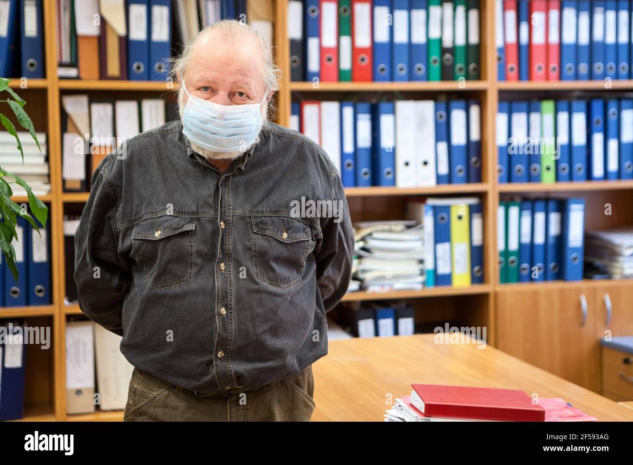 Porträt eines älteren männlichen Archivar mit Händen hinter dem Rücken Blick auf die Kamera, Mann mit Gesichtsmaske wegen Coronavirus Pandemie, Kopierraum Stockfoto