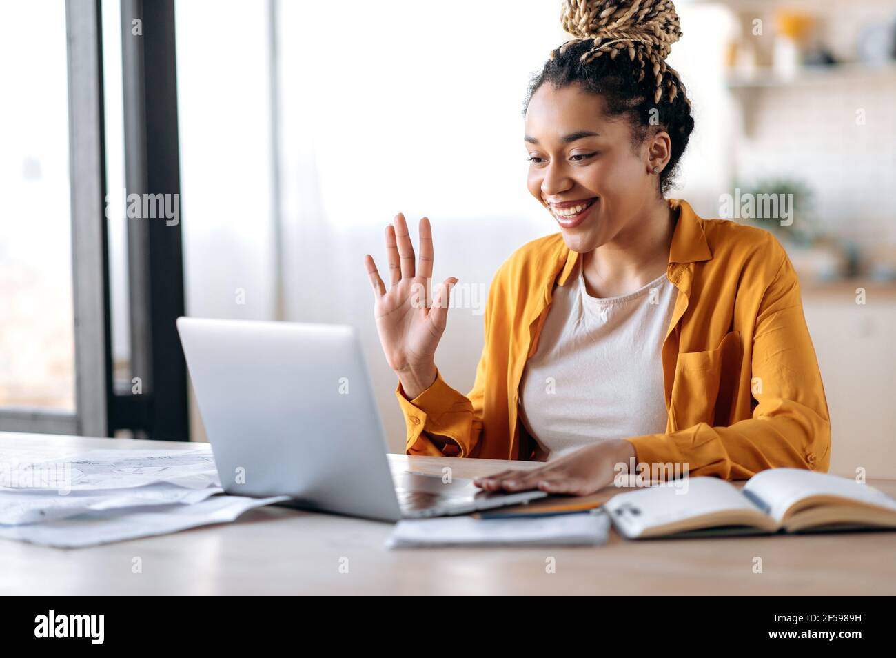 Online-Videokommunikation. Fröhliche attraktive afroamerikanische Frau, Freiberufler oder Student, in Freizeitkleidung, nutzt Laptop für Online-Videokonferenz mit Kollegen oder Freunden, grüßt, lächelt Stockfoto