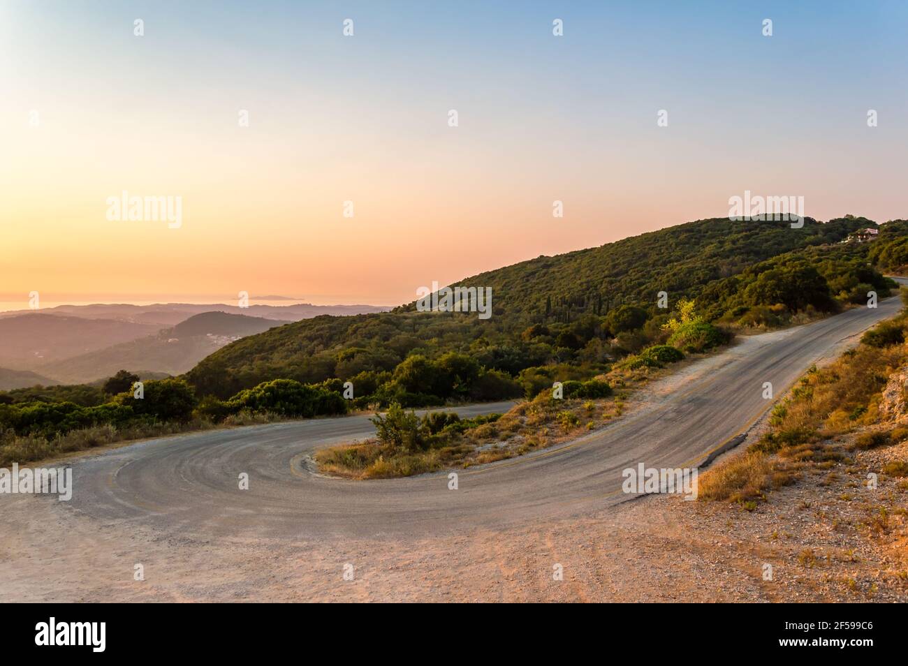 Kurvenreiche Bergstraßenkurve auf der Insel Korfu in Griechenland bei Sonnenuntergang. Schöne Landschaft Blick auf Hügel und Berge mit üppiger Vegetation über dem Meer Stockfoto