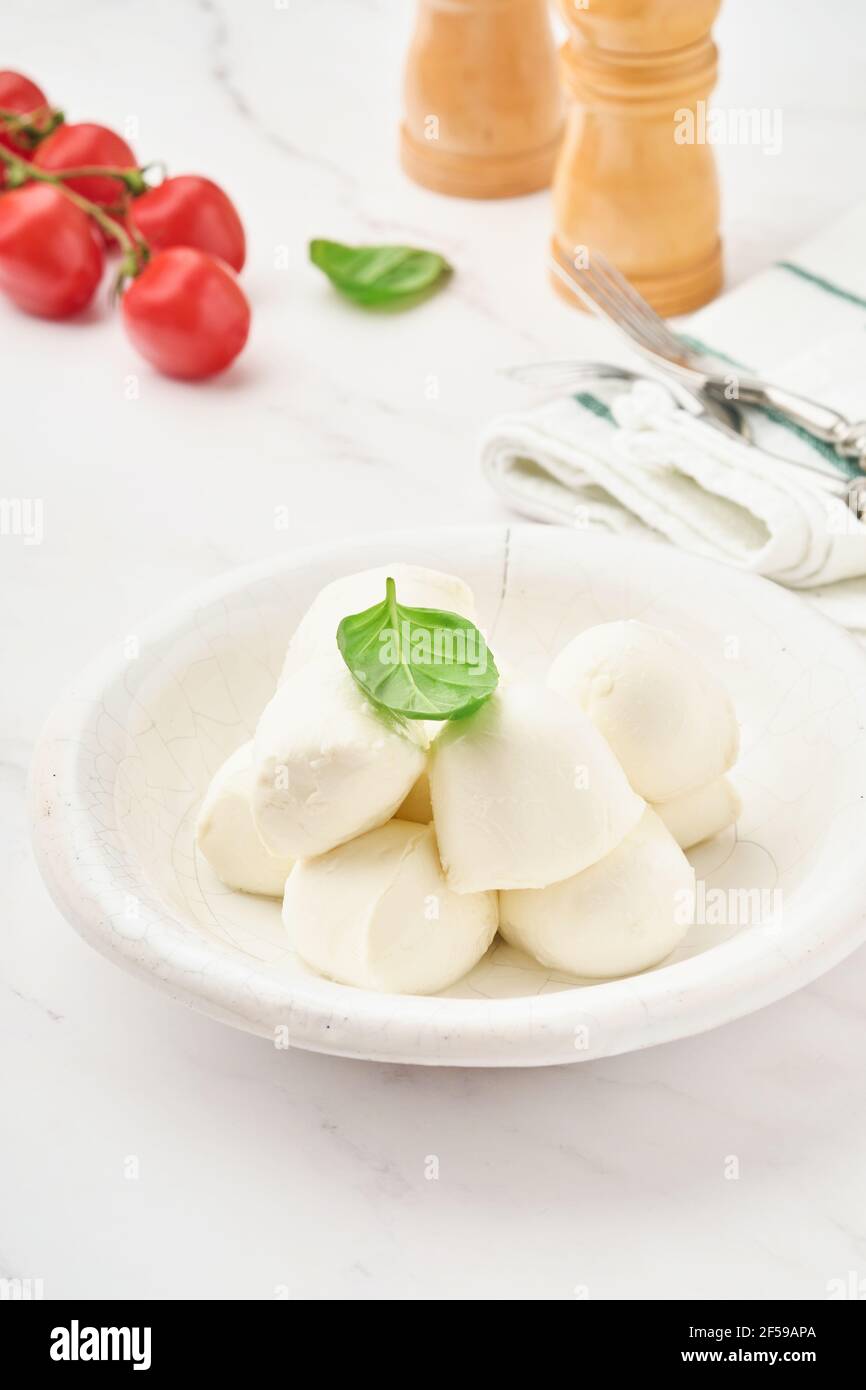 Mozzarella Käse mit Basilikum in weißer Keramikplatte und Tomatenkirsche auf Schieferstein Hintergrund, Kopierraum. Modell. Zutaten für Caprese Salat. Stockfoto