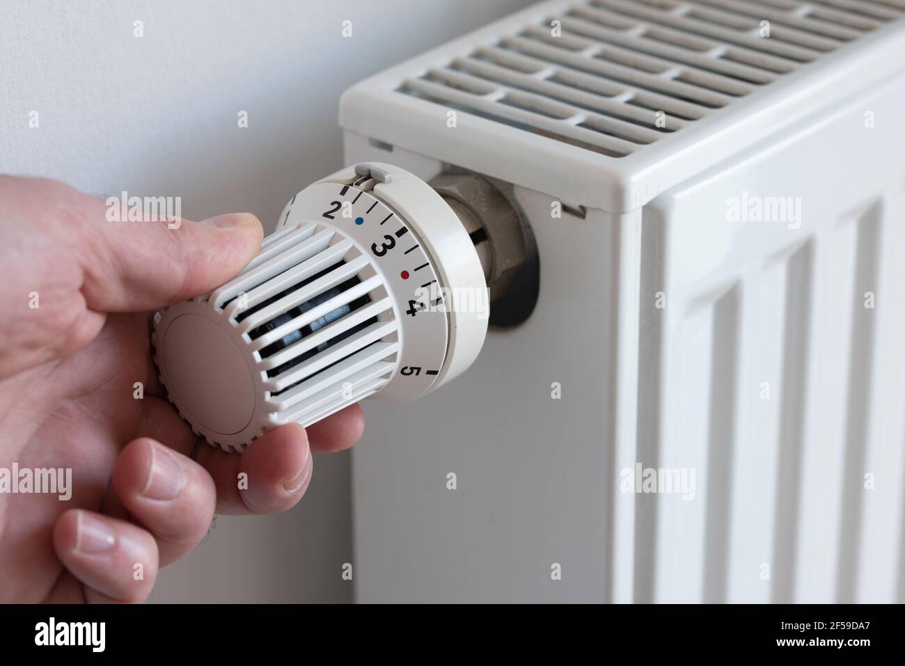 Nahaufnahme einer Person, die den Thermostat auf der Heizung herunterdreht, um zu sparen Energie Stockfoto