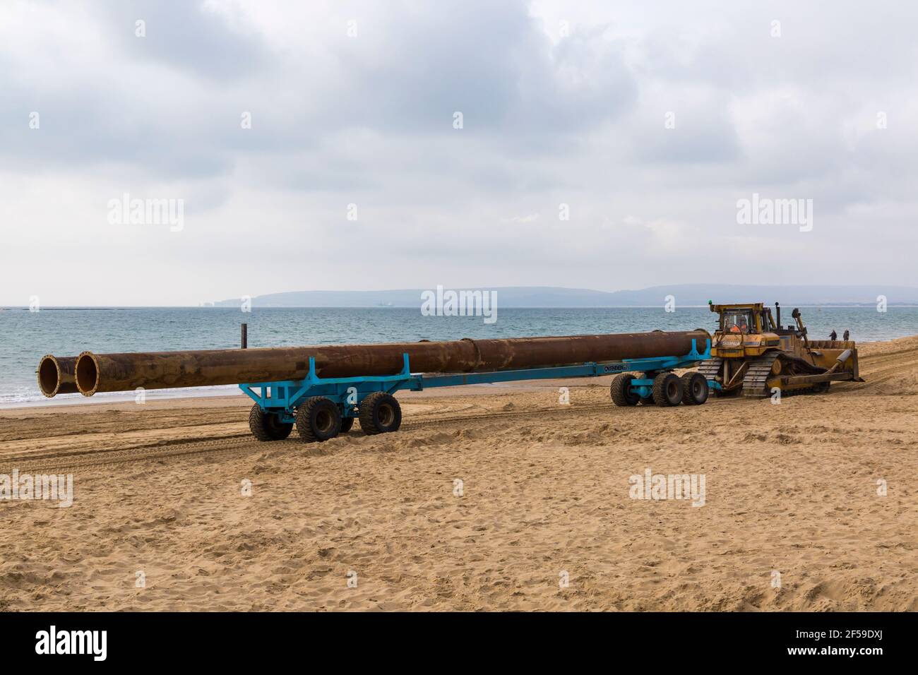 CAT Caterpillar D7H Series II Transport von großen Rohren auf Anhänger entlang Strand für Strand Nachschub Arbeit in Bournemouth und Poole Beaches, Dorset UK Stockfoto