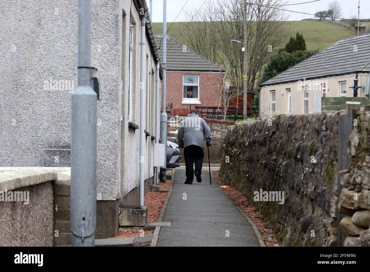 Sanquhar, Dumfries & Galloway, Schottland, Großbritannien. 22 März 2021. Alter Mann mit Gehstock, der den Gang hinauf geht. Auf dem Weg nach Hause Stockfoto
