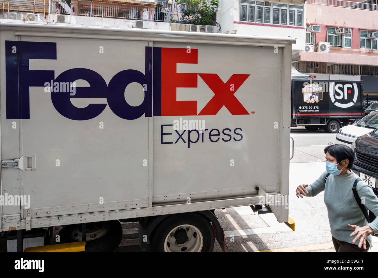 Hongkong, China. März 2021, 25th. American FedEx Express Lieferung und chinesische multinationale Lieferdienste und Logistikunternehmen LKW in Hongkong gesehen, wie ein Fußgänger an ihnen vorbeigeht. (Foto von Budrul Chukrut/SOPA Images/Sipa USA) Quelle: SIPA USA/Alamy Live News Stockfoto