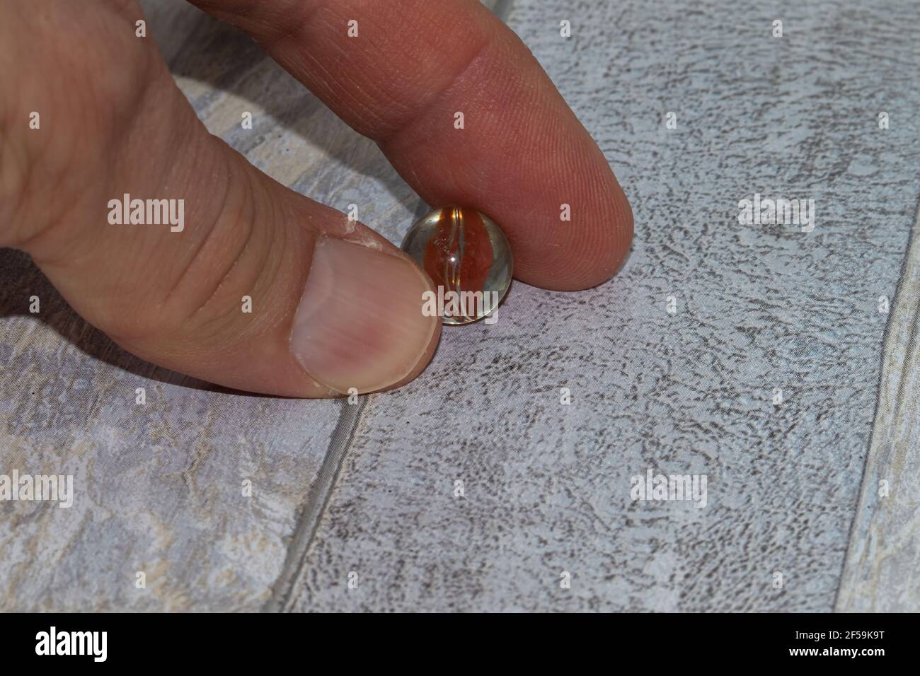 Glassmarmor mit Fingern auf Holzhintergrund gehalten Stockfoto