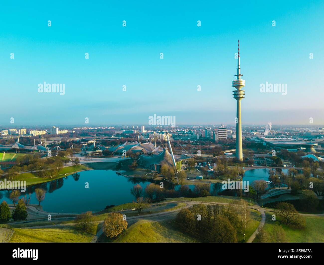 MÜNCHEN, DEUTSCHLAND - 25. März 2021: Drohne fliegt morgens bei Sonnenaufgang über dem Olympiapark München. Luftaufnahme des Sees, Olympic Tower und Olym Stockfoto