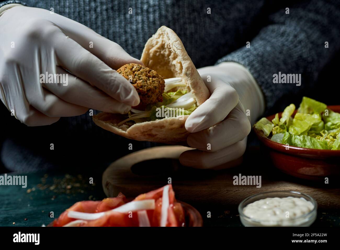 Nahaufnahme eines jungen Mannes, der Latexhandschuhe trägt und ein Falafel-Sandwich in einem Pita-Brot vorbereitet Stockfoto