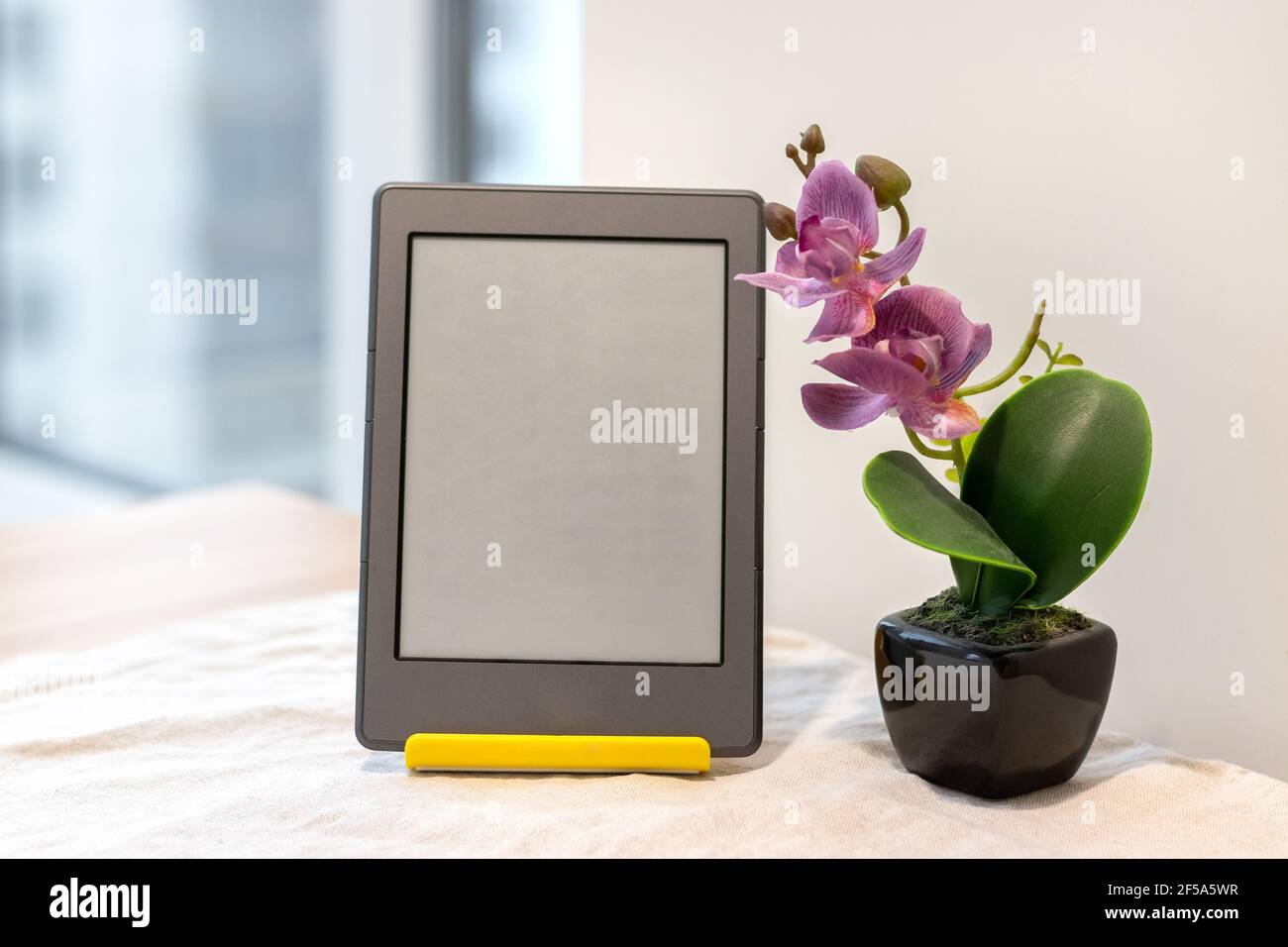 Modernes graues E-Reader elektronisches Buch mit leerem Bildschirm Ein gelber Ständer neben einer künstlichen rosa Orchidee Der Küchentisch Stockfoto
