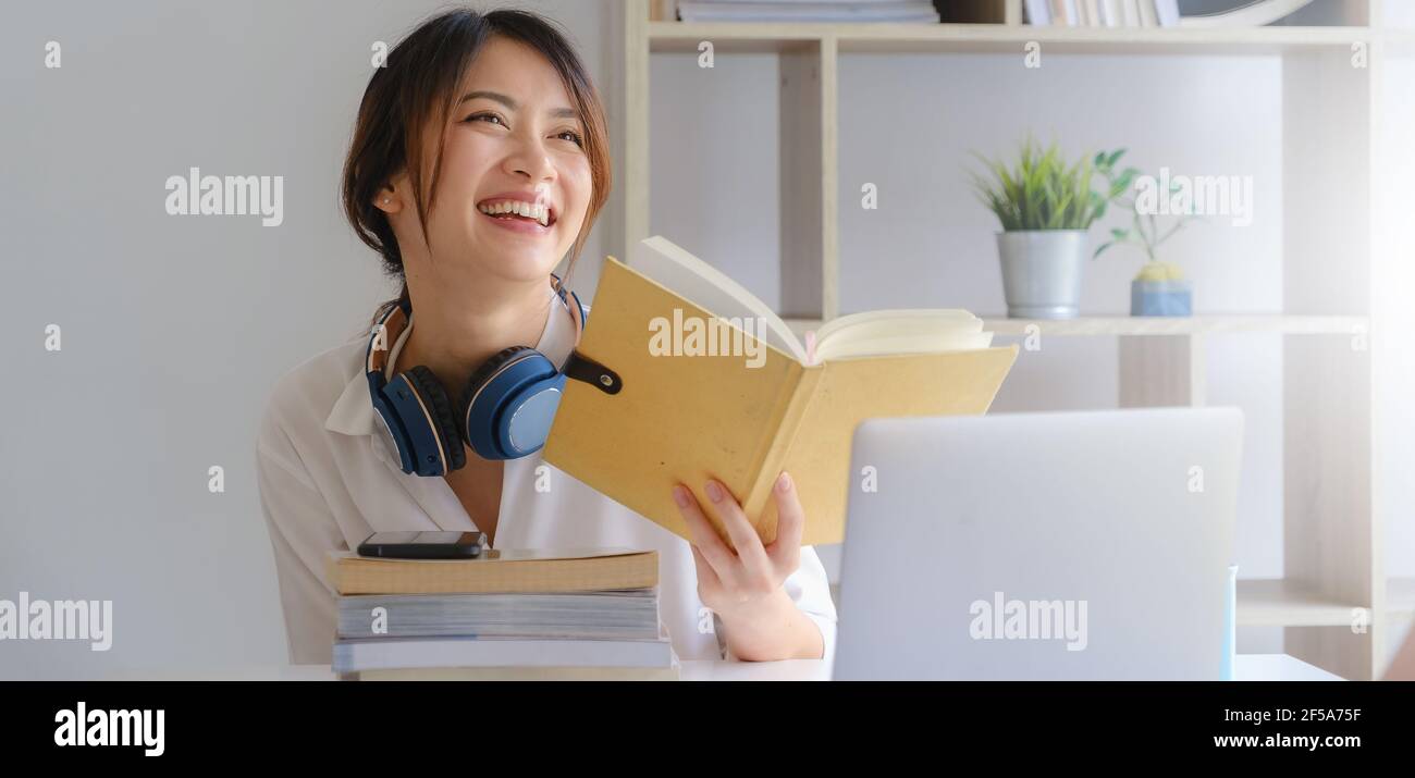 Portrait von lächelnd asiatische Student Mädchen und das Lesen eines Buches auf homeschool vor dem Lernen virtuelle Internet Online-Klasse. Covid Pandemie. Stockfoto