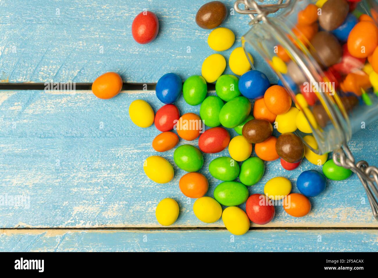 Bunte Schokoladen-Kugeln in Glas gefallen in blauen Holzhintergrund.Bonbons mehrfarbige Ansicht von oben mit Kopierraum. Stockfoto