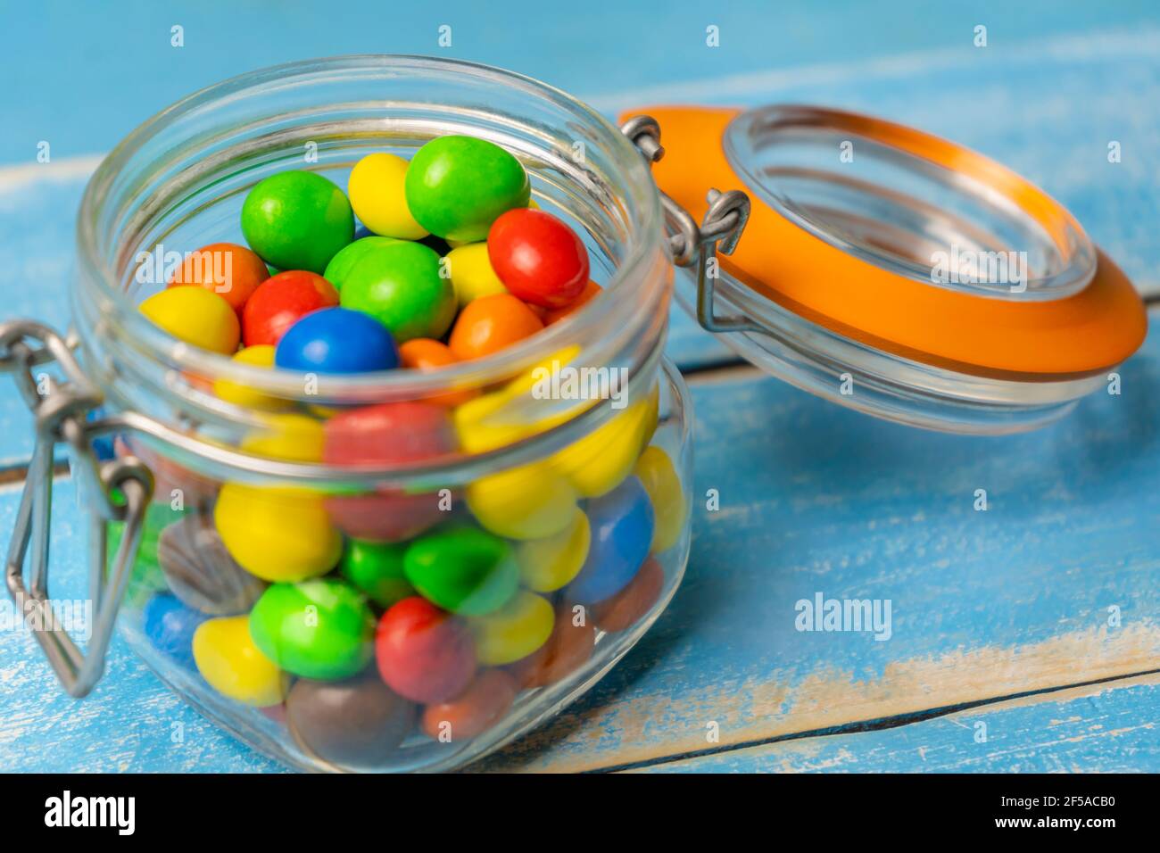 Bunte Schokoladenkugeln im Glas auf blauem Holzhintergrund.Bunte Süßigkeiten und Bonbons Hintergrund. Stockfoto